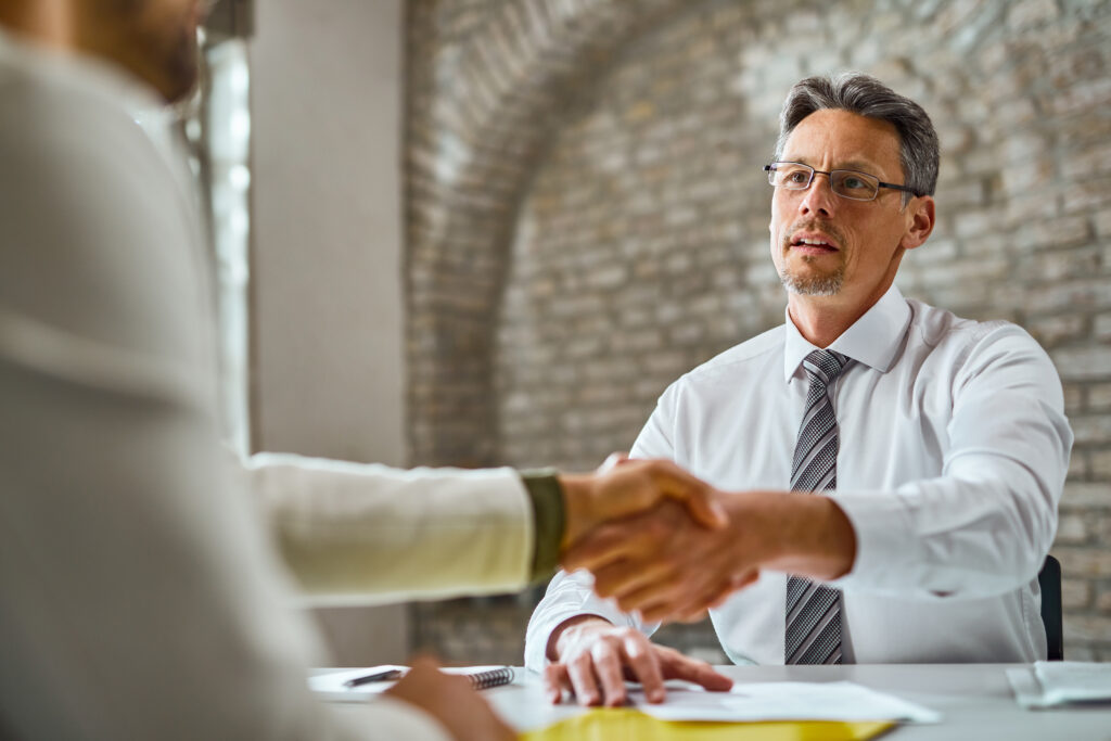 mid adult manager shaking hands with candidate during job interview office